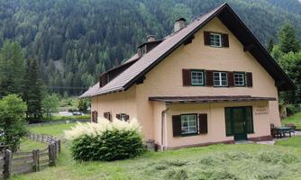 A charming house amidst green landscape and mountains. Surrounded by trees and a well-kept lawn.