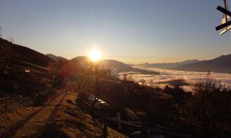 A picturesque mountain landscape with the rising sun in the background. Fog hovers over the valley, creating a tranquil atmosphere.