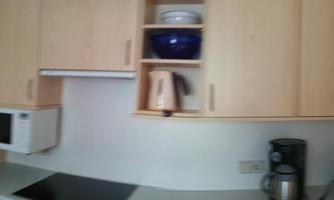 A modern kitchen with light wood cabinets and a clear countertop. The amenities include a microwave, kettle, and coffee machine.