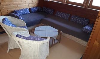 A cozy room with a large couch and two white chairs. The wooden wall and the windows provide a rustic atmosphere.