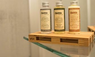 Three bottles of shampoo, shower gel, and body lotion are placed on a wooden shelf. They are arranged in a modern bathroom.
