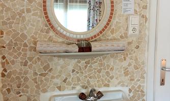 A modern sink with a round mirror on a decorative stone wall. The room is bright and inviting.