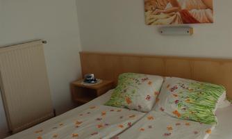 A cozy bedroom with a large bed and colorful bed linens. A decorative picture hangs on the wall.