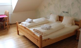 A bright room with a double bed and fresh towels. There is a wooden table and chairs and a pleasant atmosphere.