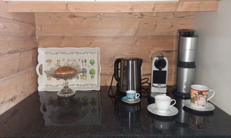 An elegant kitchen corner with wooden cladding and a black countertop. There is a coffee pot, a coffee machine, and pretty cups on a tray.
