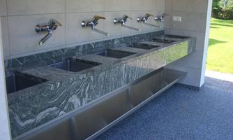 A modern washing facility with multiple sinks and an elegant, marbled basin. The room is bright and offers a clear view outside.