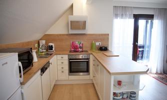 A modern kitchen with a wooden countertop and white cabinets. It includes a stove, microwave, and refrigerator.
