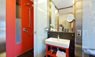 A modern bathroom with a red wall and elegant fixtures. There is a shower, a sink, and stylish accents in black and white.