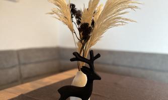 A stylish arrangement featuring a black reindeer figure and a vase filled with dried flowers. The background shows a cozy seating area.