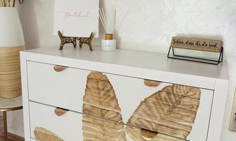 A modern dresser with golden leaf patterns on the front. In the background, decorative elements and a wall with a slightly textured surface can be seen.