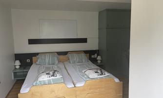 A bright bedroom with two single beds and green bedding. There is a wardrobe and nightstands with lamps.