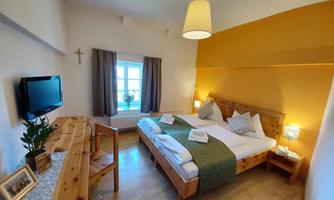 A cozy room with two beds, wooden furniture, and a television. There is a large window that lets in a lot of light, as well as a pleasant color scheme.