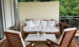 A cozy terrace with a sofa and two wooden chairs. The view of the green surroundings creates a relaxed atmosphere.