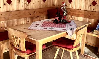 A rustic wooden table with red seats in a cozy room. On the table lies a decorative tablecloth and a small bouquet of flowers.