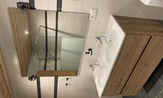 A modern bathroom with a double wooden sink and a large mirror. The walls are designed with white tiles and decorative black stripes.