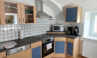 A modern kitchen with light wooden cabinets and blue accents. The amenities include a stove, a microwave, and a coffee maker.