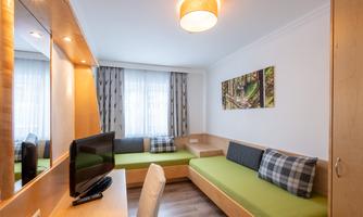 A cozy room with bright interior and a green seating area. A picture of a forest hangs on the wall.