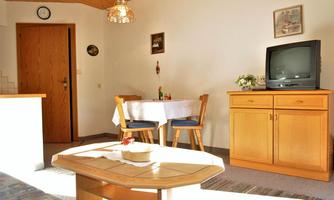 A cozy living space with a table and chairs. In the background, there is a TV and a nice sideboard.