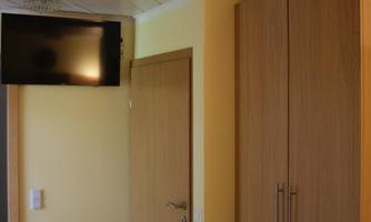 A bright room with a wooden cabinet and a TV on the wall. The walls are painted in gentle shades of yellow.