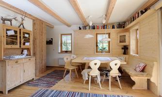 A cozy dining area with wooden furniture and a table in a modern alpine style. The walls are light and there are large windows that let in a lot of light.