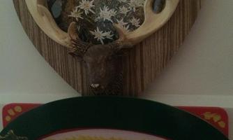 A decorative heart-shaped wall plaque featuring a noble alpine garden and a deer antler. Below it is a sign that reads "EDELWEISS."