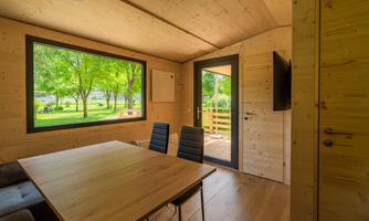 A modern, bright room with wooden paneling and a large window overlooking a green garden. There is a table and chairs that create an inviting atmosphere.