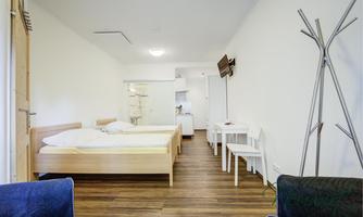 A simple and modern room with two beds and minimalist furniture. There is a table and chairs as well as access to a small kitchen.