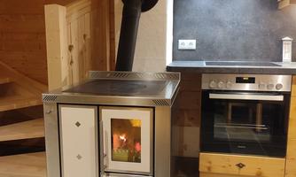 A modern wood stove in a cozy kitchen with wood paneling. In the background, there is a stove and an integrated wall.