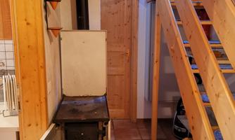 A cozy corner with an old stove and a wood basket. In the background, you can see a wooden staircase.