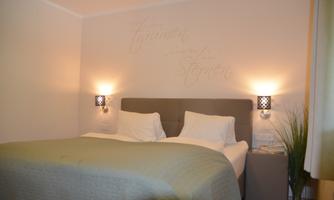 A modern bedroom with a double bed and soft lighting. An inspiring quote is on the wall, and there is a small plant next to the nightstand.