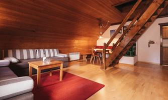 A cozy living space with wooden paneling and an attractive staircase. The furnishings include a couch, a wooden table, and chairs.