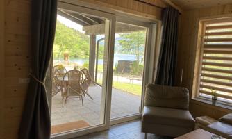 A cozy wooden terrace overlooking a lake. The large facade of windows lets in plenty of light and offers a beautiful view of nature.