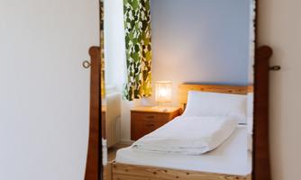 A cozy bedroom with a wooden bed and a lamp. The mirror reflects green curtains and a blue wall.