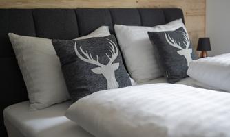 A cozy bedroom with a bed and decorative pillows. The pillows feature a stylized antler pattern and add a rustic touch.