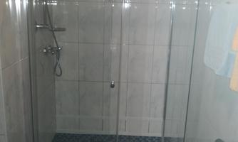 A modern shower cabin with glass walls and silver fittings. The floor is tiled with blue tiles.