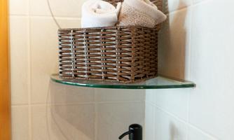 An elegant bathroom shelf with a towel and a liquid soap dispenser. There is a rattan basket and a decorative bowl.
