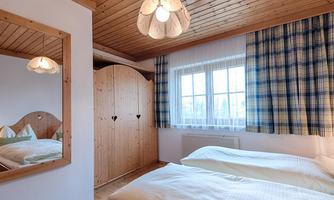 A cozy bedroom with two single beds and wooden furniture. Large window with curtains and a mirror on the wall.