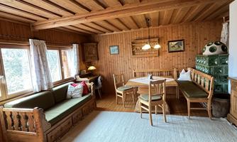 A cozy room with wooden walls and windows that let in plenty of daylight. There is a seating area and a dining table with chairs.