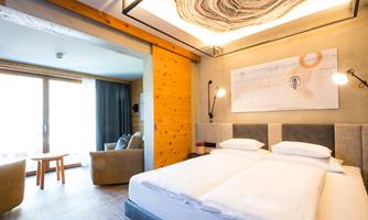 A modern hotel room with a double bed and a cozy seating area. Large windows provide plenty of natural light and an inviting atmosphere.