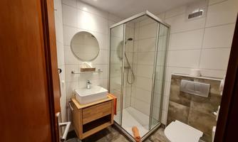 A modern bathroom with a glass shower cubicle and an elegant sink. The walls are light tiled, and the atmosphere is friendly and inviting.