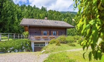 A cozy wooden house surrounded by green meadows and trees. The sky is clear and it is a beautiful day.