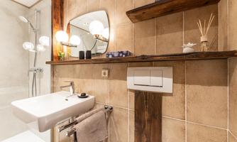 A modernly furnished bathroom with a sink, a large mirror, and stylish wooden shelves. The warm tones and lighting create an inviting atmosphere.