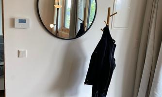 A modern entrance area with a round mirror and a hook for clothing. On the stool, there is a gray piece of furniture for seating.