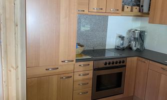 A modern kitchen with wooden cabinets and a bright countertop. It is well-equipped with a stove and various kitchen appliances.