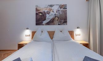 A cozy bedroom with two single beds and modern bedside lamps. A picture of cows hangs on the wall, creating a rural atmosphere.