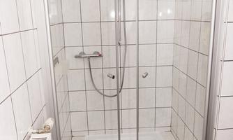 A modern shower with a glass partition and white tiled wall. A chair stands next to the shower on the floor.