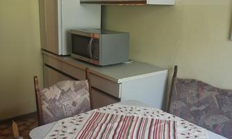 A simple kitchen with a table and chairs. In the background, there is a refrigerator and a microwave.