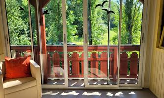 A bright veranda with large French doors and a view of a green garden. A cozy armchair with an orange cushion sits next to it.