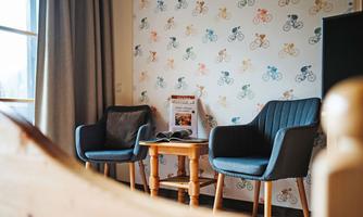 A cozy room with two blue armchairs and a small table. The wall is decorated with colorful bicycle patterns.