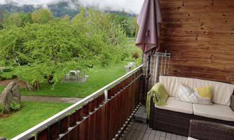 A cozy balcony with seating. In the background, green landscape and trees can be seen.